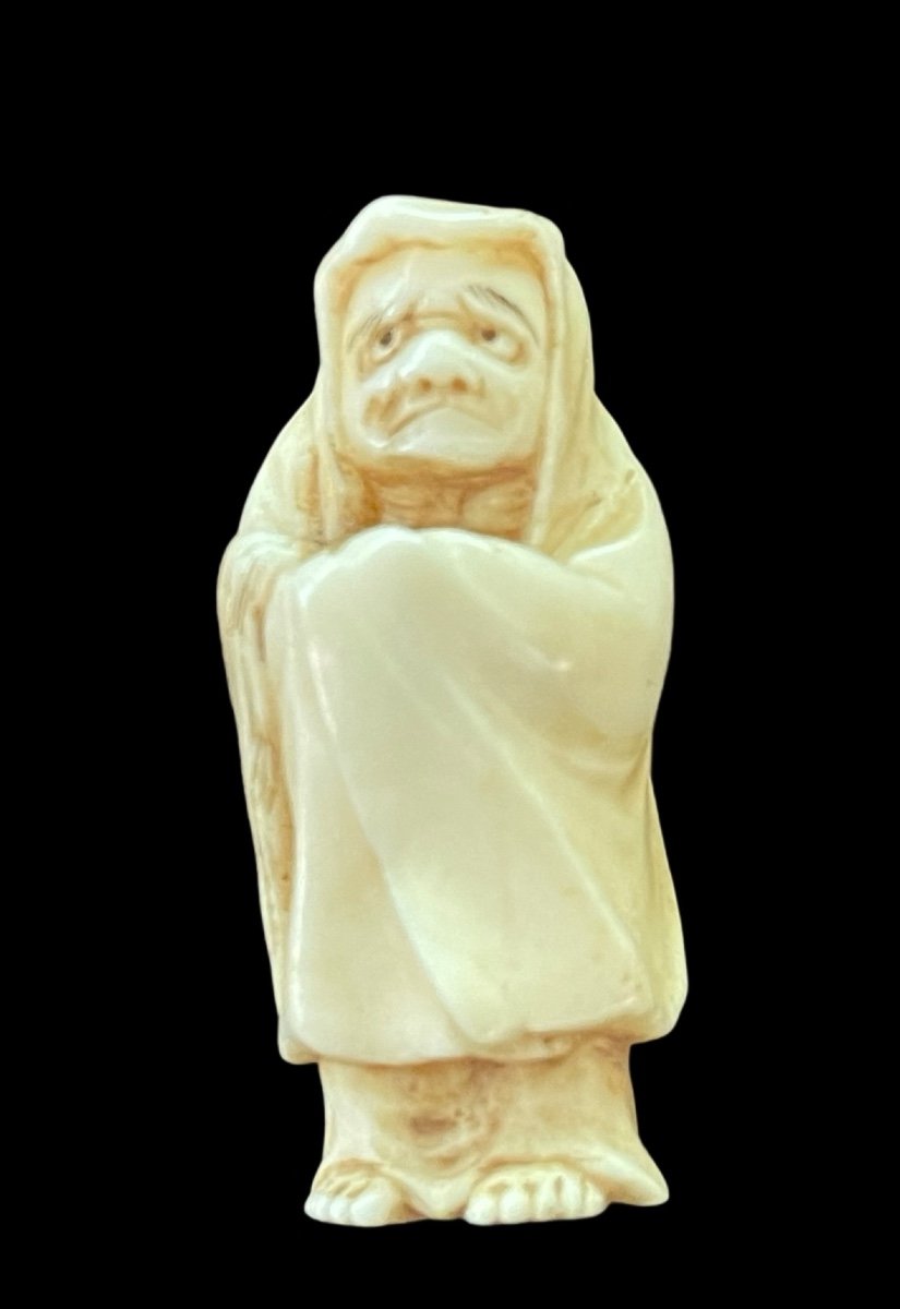 Netsuke in avorio raffigurante personaggio maschile con mantello.Giappone.