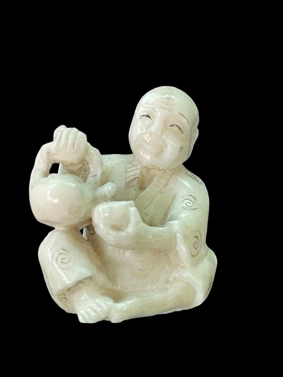 Netsuke in avorio raffigurante personaggio maschile seduto che versa il the'.