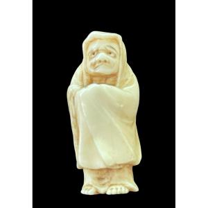 Netsuke in avorio raffigurante personaggio maschile con mantello.Giappone.