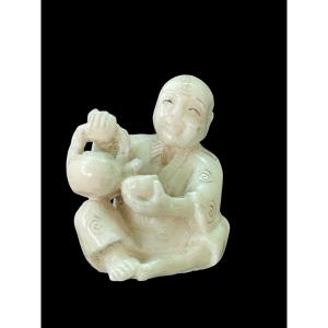 Netsuke in avorio raffigurante personaggio maschile seduto che versa il the'.