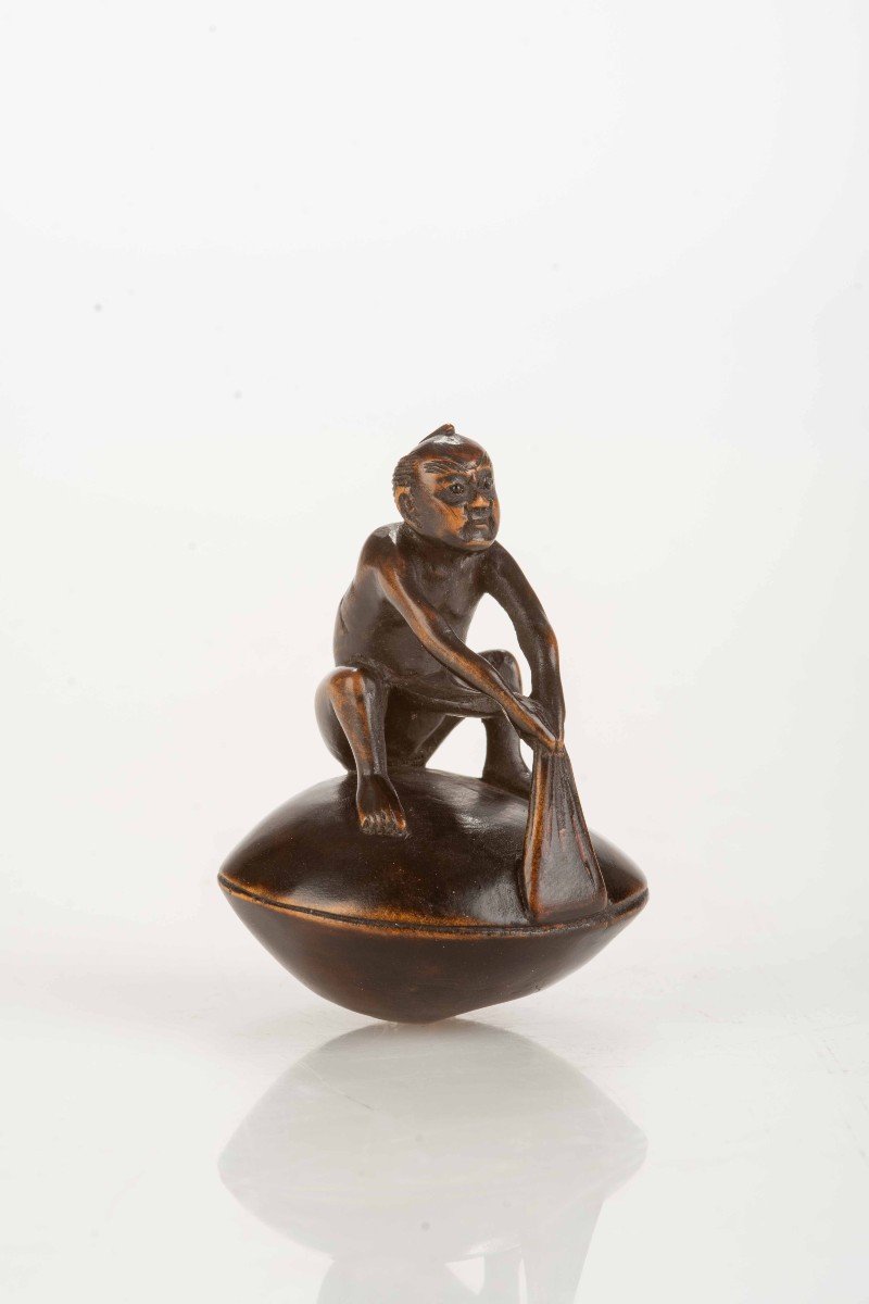 Netsuke in legno di bosso raffigurante un personaggio seduto su un hamaguri gigante 