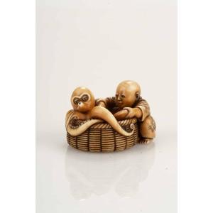 Netsuke in avorio raffigurante un bambino accovacciato accanto a un grande cesto 